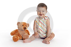 Happy Baby girl sits besides her bear toy