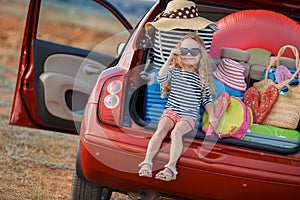 Happy baby girl sitting in the car trunk