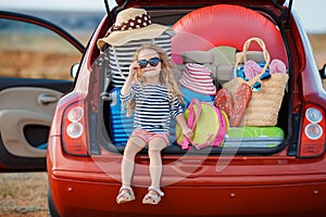 Happy baby girl sitting in the car trunk