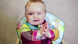 Happy baby girl sitting on children`s chair in a room and smiling, claps his hands