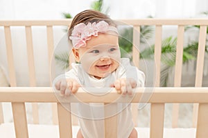 Happy baby girl six months standing in the crib