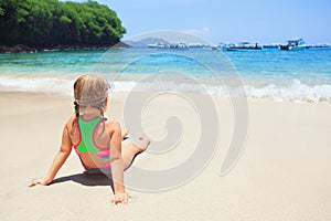 Happy baby girl in snorkeling mask sit on sand beach