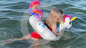 Happy baby girl swimming on an inflatable swimming unicorn in the sea