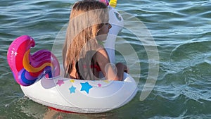 Happy baby girl swimming on an inflatable swimming unicorn in the sea