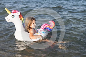 Happy baby girl swimming on an inflatable swimming unicorn in the sea