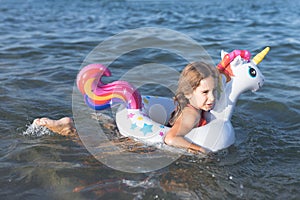 Happy baby girl swimming on an inflatable swimming unicorn in the sea