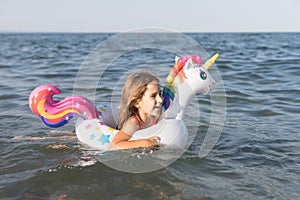 Happy baby girl swimming on an inflatable swimming unicorn in the sea