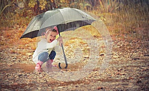 Happy baby girl with an umbrella in the rain playing on nature