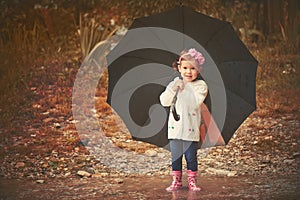 Happy baby girl with an umbrella in the rain playing on nature