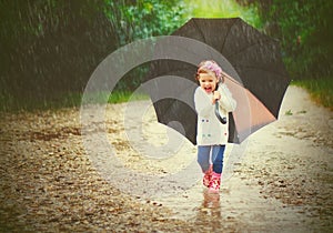 Happy baby girl with an umbrella in the rain runs through