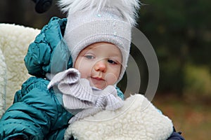 happy baby girl in warm clothes and hat covering his neck from cold wind in autumn outdoor