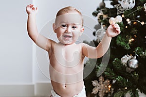 Happy baby girl wearing diaper decorating Christmas Tree