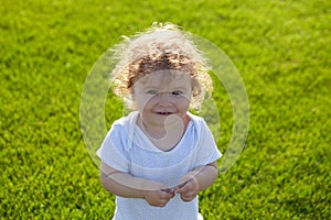 Happy baby in grass on the fieald at sunny summer evening. Smiling child outdoors. Baby face closeup. Funny little child