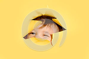 Happy baby in a hole on a paper yellow background. Torn child's head s