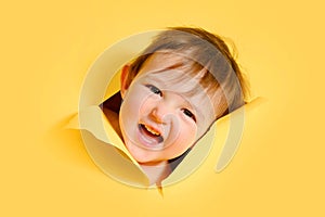 Happy baby in a hole on a paper yellow background. Torn child\'s head s