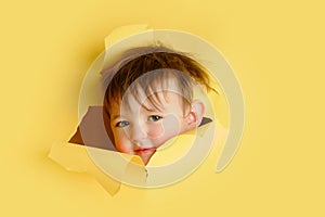 Happy baby in a hole on a paper yellow background. Torn child's head s