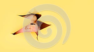 Happy baby in a hole on a paper yellow background. Torn child's head s