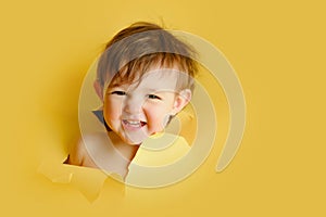 Happy baby in a hole on a paper yellow background. Torn child's head s