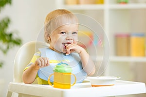 Happy baby kid boy eating itself with spoon