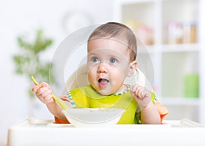 Happy baby kid eating food itself with spoon