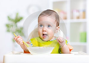 Happy baby kid eating food itself with spoon photo