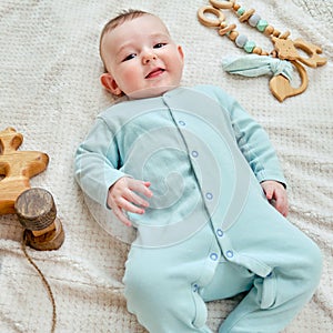 Happy baby lies on a blanket in mint color clothes with wooden toys. Smiling child in turquoise pajamas, top view