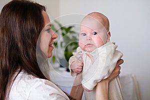 Happy baby. Little cutest serious caucasian white infant child looking at camera on mother hands. Family life, moms love