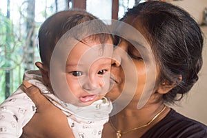 Happy Baby Loves mom Kisses. Loving Mother kissing cute little adorable kid on her lap. Close-up portrait. Indian ethnicity. Front