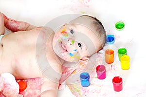 Happy baby lying among finger-type paints