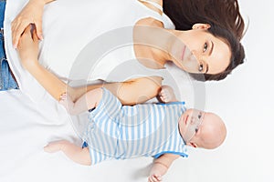 Happy baby lying near her mother on a white bed