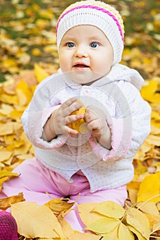 Happy baby outdoor at autumn park playing with yellow leaves