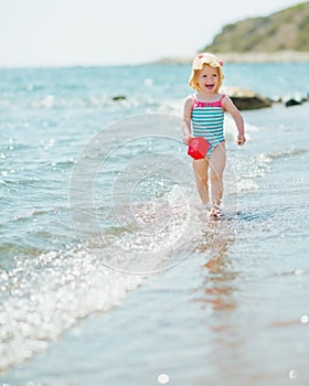 Happy baby with pail running along seashore