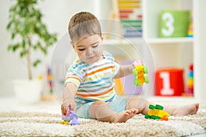 Happy baby playing with colorful plastic bricks on the floor. Toddler having fun and building a train out of constructor