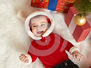 Happy baby portrait in christmas decoration, lie on fur near fir tree and gifts, winter holiday concept