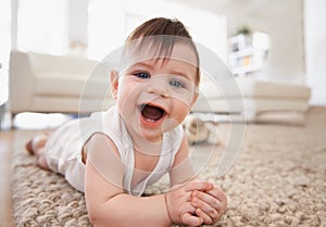 Happy, baby portrait and tummy time on floor, laugh and play in living room. Teething, child development and growth