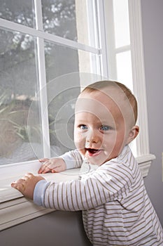 Happy baby pulling himself up on window sill