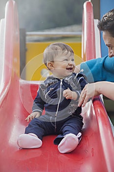 Happy baby on red slide smiling at mother