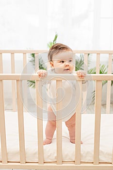 Happy baby girl six months standing in the crib