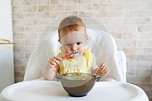 Happy baby sitting in highchair and eating greek yogurt