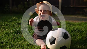 Happy Baby Sitting With Soccer Black White Classic Ball On Green Grass. Adorable Infant Baby Playing Outdoors In