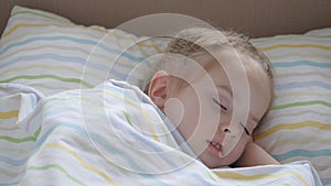 Happy baby sleeps in a baby bed and smiles. Mom put her tired daughter to bed. A cute child is resting in the nursery in