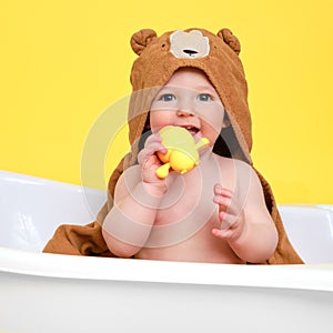 Happy baby toddler boy is sitting in a white bathtub on a studio yellow