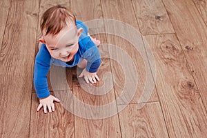 Happy baby toddler crawls on a wooden laminate. Funny child on the parquet in the home living room, aged 6-11 months
