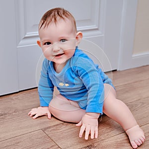 Happy baby toddler crawls on a wooden laminate. Funny child is sitting smiling on the parquet in the home living room, aged 6-11