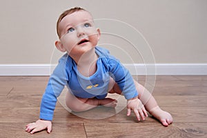 Happy baby toddler crawls on a wooden laminate. Funny child is sitting smiling on the parquet in the home living room, aged 6-11