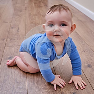 Happy baby toddler crawls on a wooden laminate. Funny child is sitting smiling on the parquet in the home living room, aged 6-11