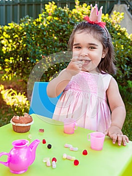 Happy baby toddler girl, eating gummies laughing and smiling in outdoor tea party