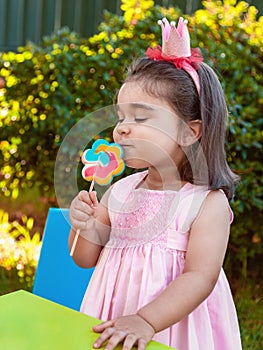 Happy baby toddler girl smelling and savoring a large colorful lollipop smell, scent or aroma