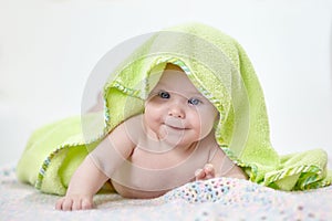 Happy baby under a green towel after bathing