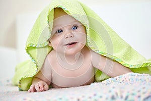 Happy baby under a green towel after bathing